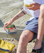 A close up of a man holding a One Green Bottle lunchbox in soldier showing the different compartments inside.