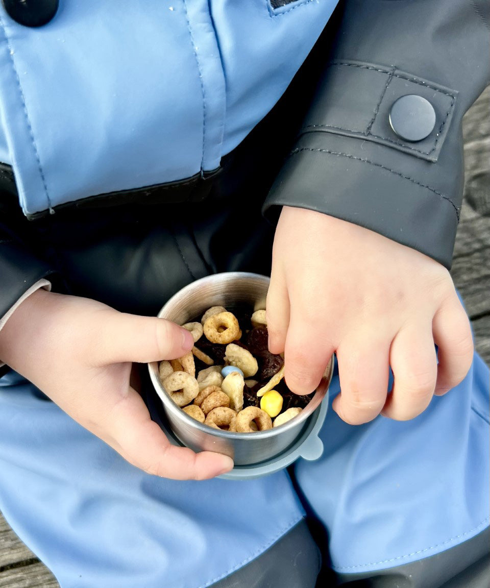 A close up of a child holding a One Green Bottle snack pot from the lunchbox set in soldier showing how much snacks can fit inside.