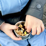A close up of a child holding a One Green Bottle snack pot from the lunchbox set in soldier showing how much snacks can fit inside.