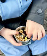 A close up of a child holding a One Green Bottle snack pot from the lunchbox set in soldier showing how much snacks can fit inside.