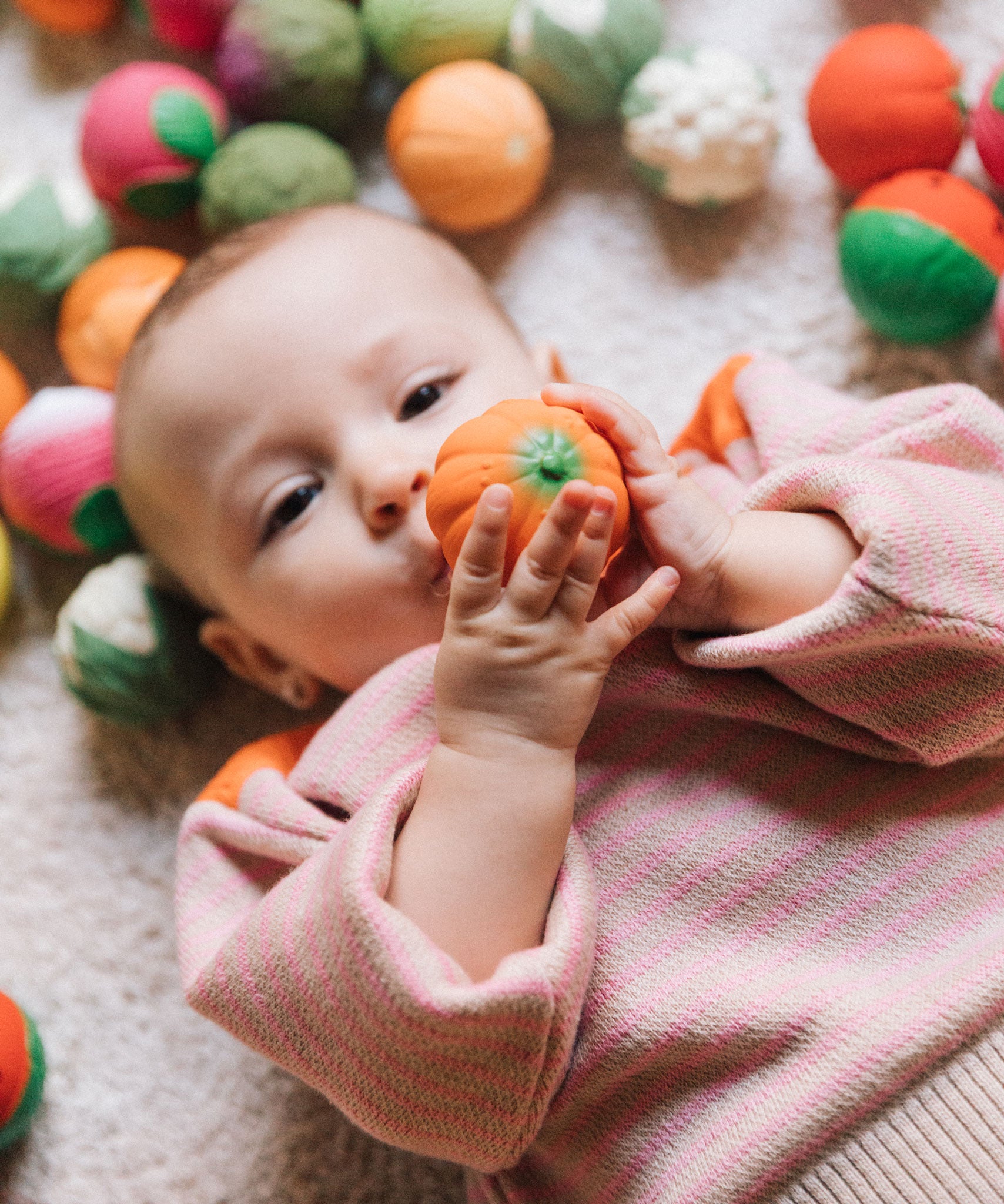 A baby grasping onto the pumpkin ball from the Oli & Carol Vegetable soup Baby Sensory Balls set