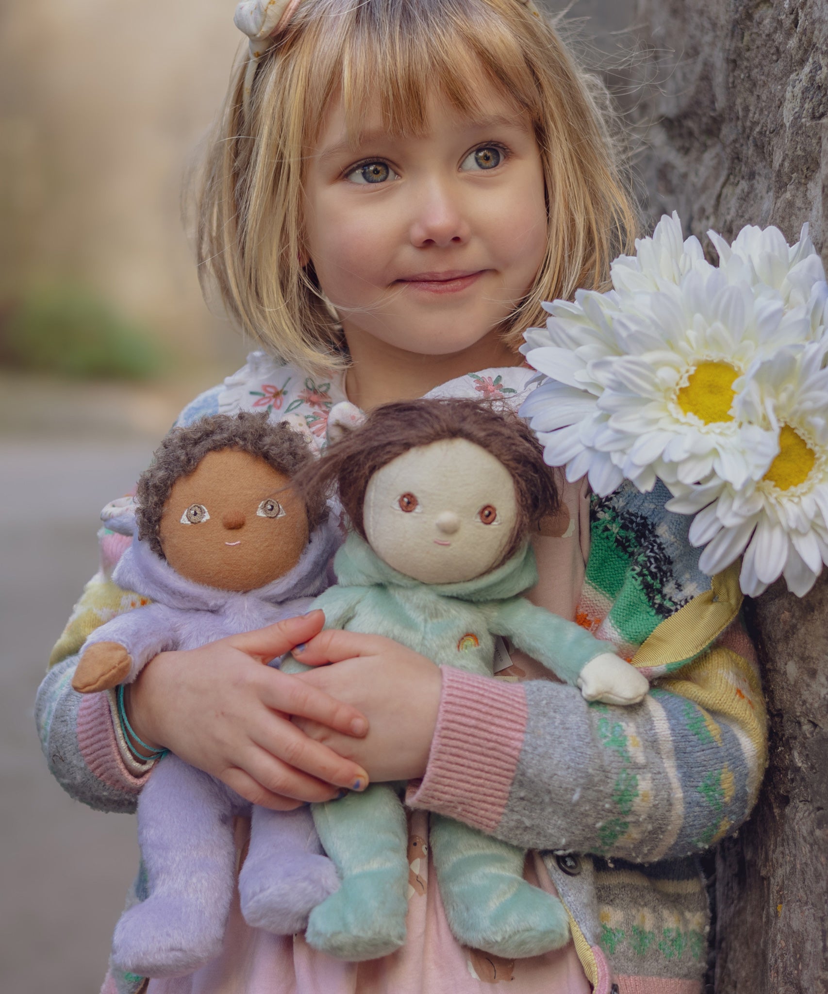 A child holding two Olli Ella Bunny Dinky Dinkum Dolls in their arms, Babs the purple bunny and  Biscuit the mint green bunny.