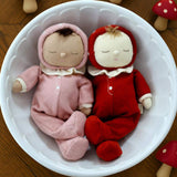 The Olli Ella Dozy Dinkum Dolls - Toadstool Pip and Moppet in a bowl together. One is in a pink onesie, and one is in a red onesie.