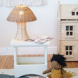 An Olli Ella Natural Rattan Mushroom Lamp placed on a small white square stool.