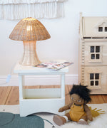 An Olli Ella Natural Rattan Mushroom Lamp placed on a small white square stool.