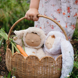 A close up of a child carrying a Natural Rattan Olli Ella Petal Basket. There are two bunny dozy dinkums and carrots inside the basket.
