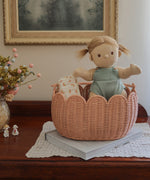 A Dinkum Doll placed in and Olli Ella Seashell Pink Petal Basket.
