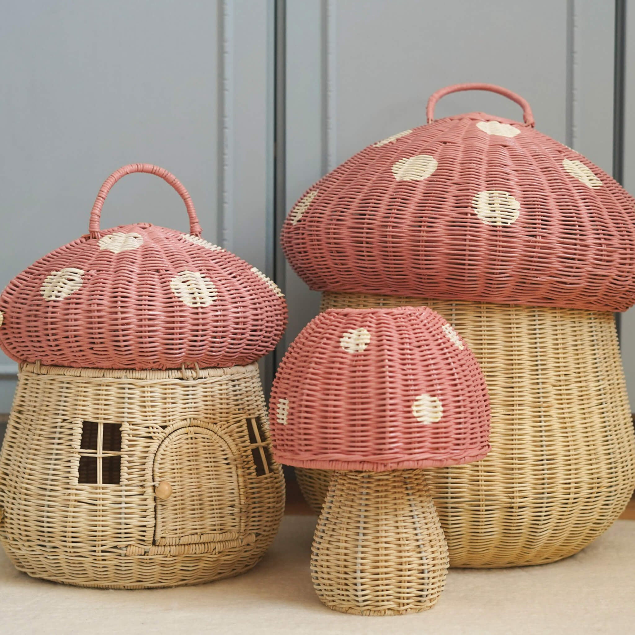 The Olli Ella rattan toadstool lamp with a natural base and a pink mushroom top, with two toadstool baskets in the same style.