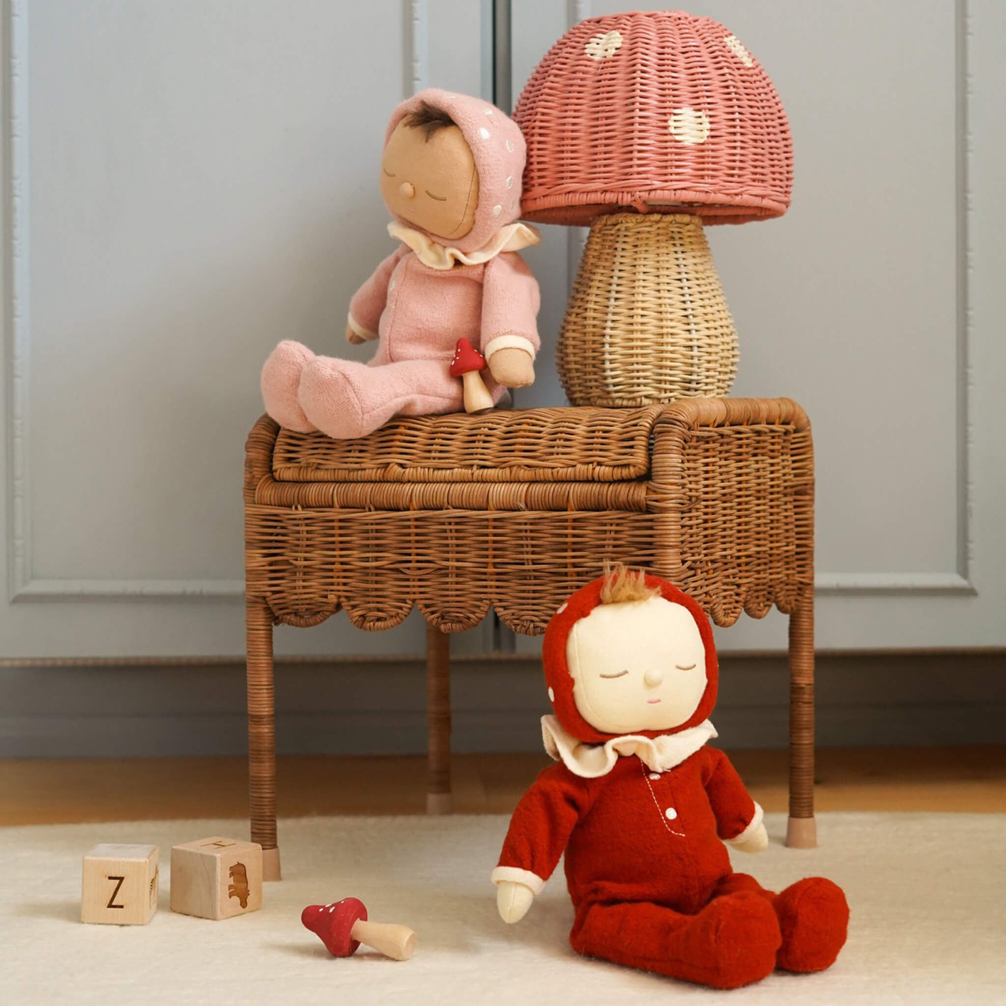 The Olli Ella rattan toadstool lamp with a natural base and a pink mushroom top, on a table with dinkum dolls.