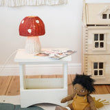 An Olli Ella Rattan Toadstool Lamp placed on a square wooden stool.