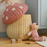 The Olli Ella large woven rattan storage basket, in the shape of a mushroom with a spotty pink toadstool lid, a dozy doll is leaning against it.
