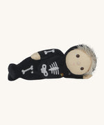 Olli Ella Scully Skeleton Dinky Dinkum Doll soft toy laying on it's side. The doll features glow in the dark bone details on the front along with a small embroidered rainbow on the chest. These soft toys are part of Olli Ella's Halloween collection available here at Babipur.