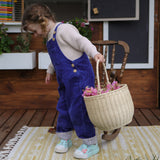 A child holding an Olli Ella Large Strw Rattan Gathering basket in their hand filled with flowers.