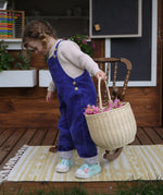 A child holding an Olli Ella Large Strw Rattan Gathering basket in their hand filled with flowers.