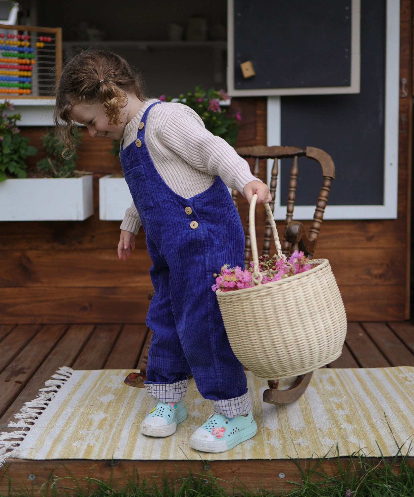 A child holding an Olli Ella Large Strw Rattan Gathering basket in their hand filled with flowers.