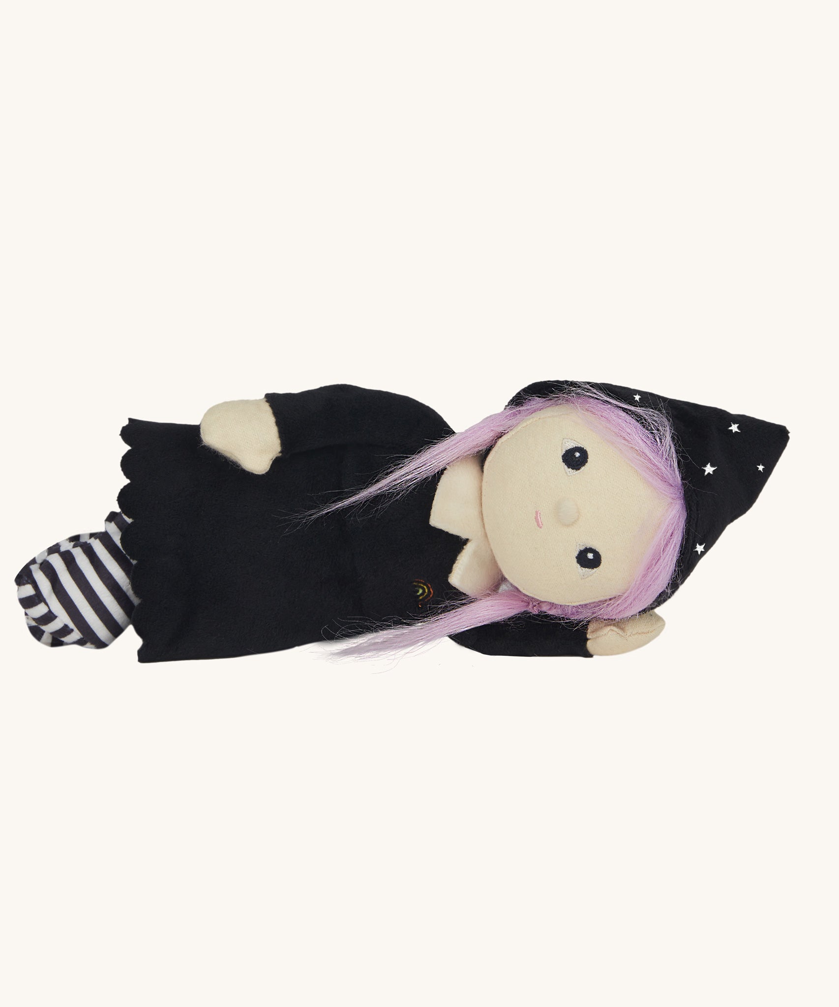 An Olli Ella Willa Witch Dinky Dinkum Doll laying on it's side. A witch with a black outfit and matching hat with glow in the dark features on the striped tights, collar ans tars on the hat. These soft toys are part of Olli Ella's Halloween collection available here at Babipur.