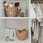 The Olli Ella Rattan Lily Basket Set in Seashell Pink on shelves in a wardrobe. The larger basket is holding Dozy Dinkum dolls on the top shelf