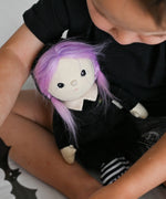A child holding the Olli Ella Willa Witch Dinky Dinkum Doll. A witch with a black outfit and matching hat with glow in the dark features on the striped tights, collar and stars on the hat. These soft toys are part of Olli Ella's Halloween collection available here at Babipur.