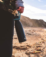 Close up of hand holding a One Green Bottle life collection canteen on a sunny beach