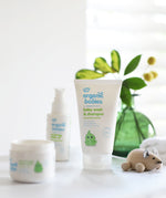 Organic Babies Baby Wash & Shampoo Scent Free placed on a white surface next to a wooden toy mouse. Other products from the organic babies collection can be seen in the background.