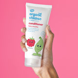 Organic Children Berry Smoothie Conditioner in an adult's hand pictured against a bright pink background.