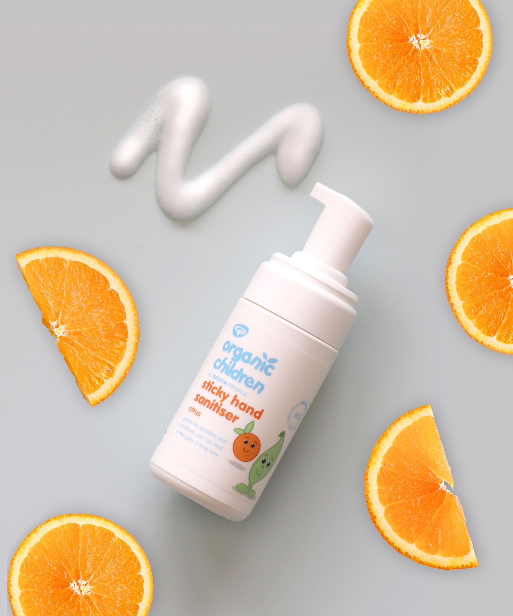 Organic Children sticky hands sanitiser on a light green background with some of teh product on the surface with slices of oranges.
