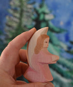 A pink coloured Ostheimer little angel held in an adult's hand to show scale. This wooden figure is part of a large range of expertly hand crafted, Waldorf inspired, wooden toys here at Babipur.