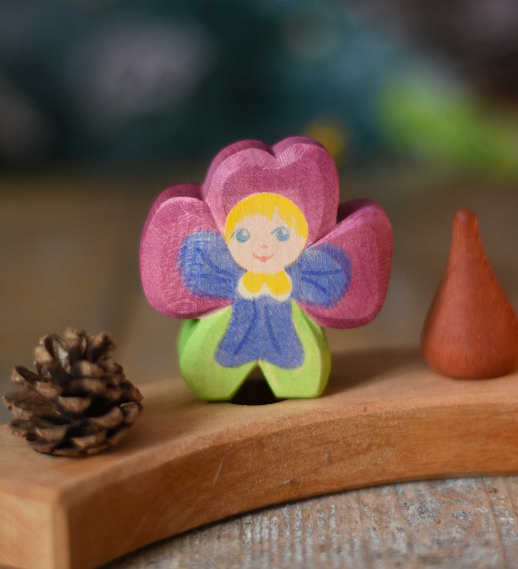 An Ostheimer hand made and hand painted wooden pansy Flower Child figure toy placed on a natural Grimm's celebration ring. These flower child wooden figures are part of a wide range of expertly hand crafted wooden toys here at Babipur.