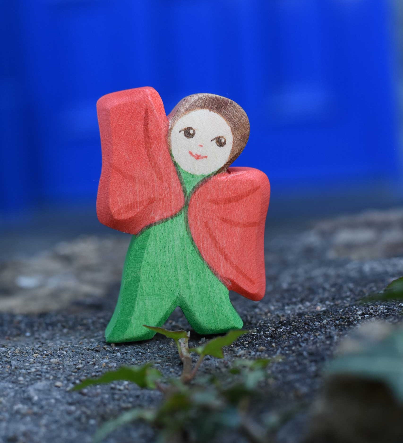 An Ostheimer hand made and hand painted wooden poppy Flower Child figure toy placed on a stone wall outdoors. These flower child wooden figures are part of a wide range of expertly hand crafted wooden toys here at Babipur.