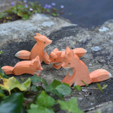 A family of four Ostheimer wooden Fox figures placed on a stone wall outdoors. Check out our full range of expertly crafted wooden toy figures and scenery here at Babipur.