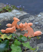 A family of four Ostheimer wooden Fox figures placed on a stone wall outdoors. Check out our full range of expertly crafted wooden toy figures and scenery here at Babipur.