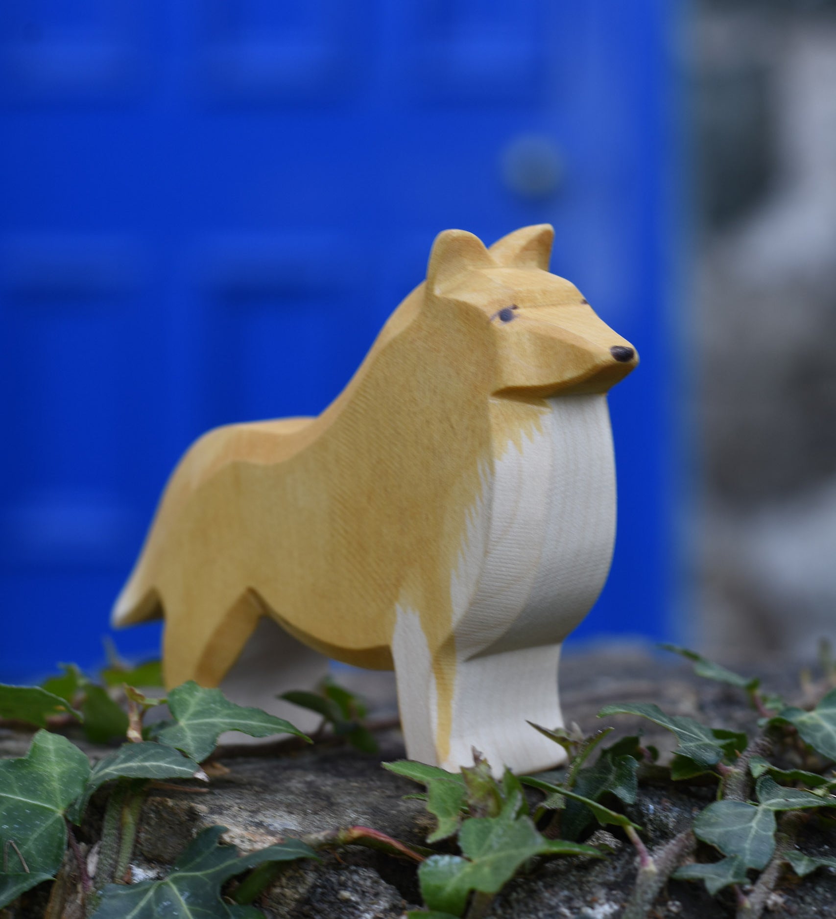 An Ostheimer Collie Dog Handmade Wooden Toy placed on a stone wall outdoors. These wooden figures are part of a large range of expertly hand crafted, Waldorf inspired, wooden toys here at Babipur.