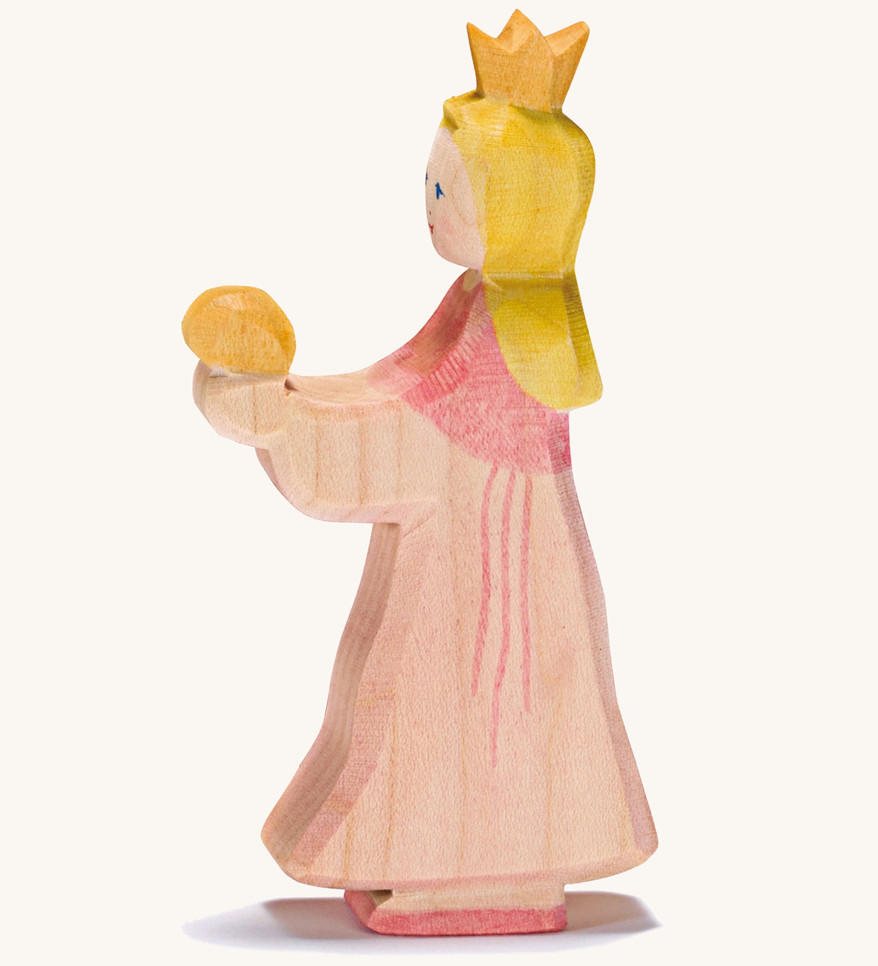 A wooden Ostheimer princess wearing a pink dress with a gold crown on her head . An Ostheimer pink princess for frog prince wooden toy figure held up in an adult's hand to show scale. This wooden figure is part of a large range of expertly hand crafted, Waldorf inspired, wooden toys here at Babipur.