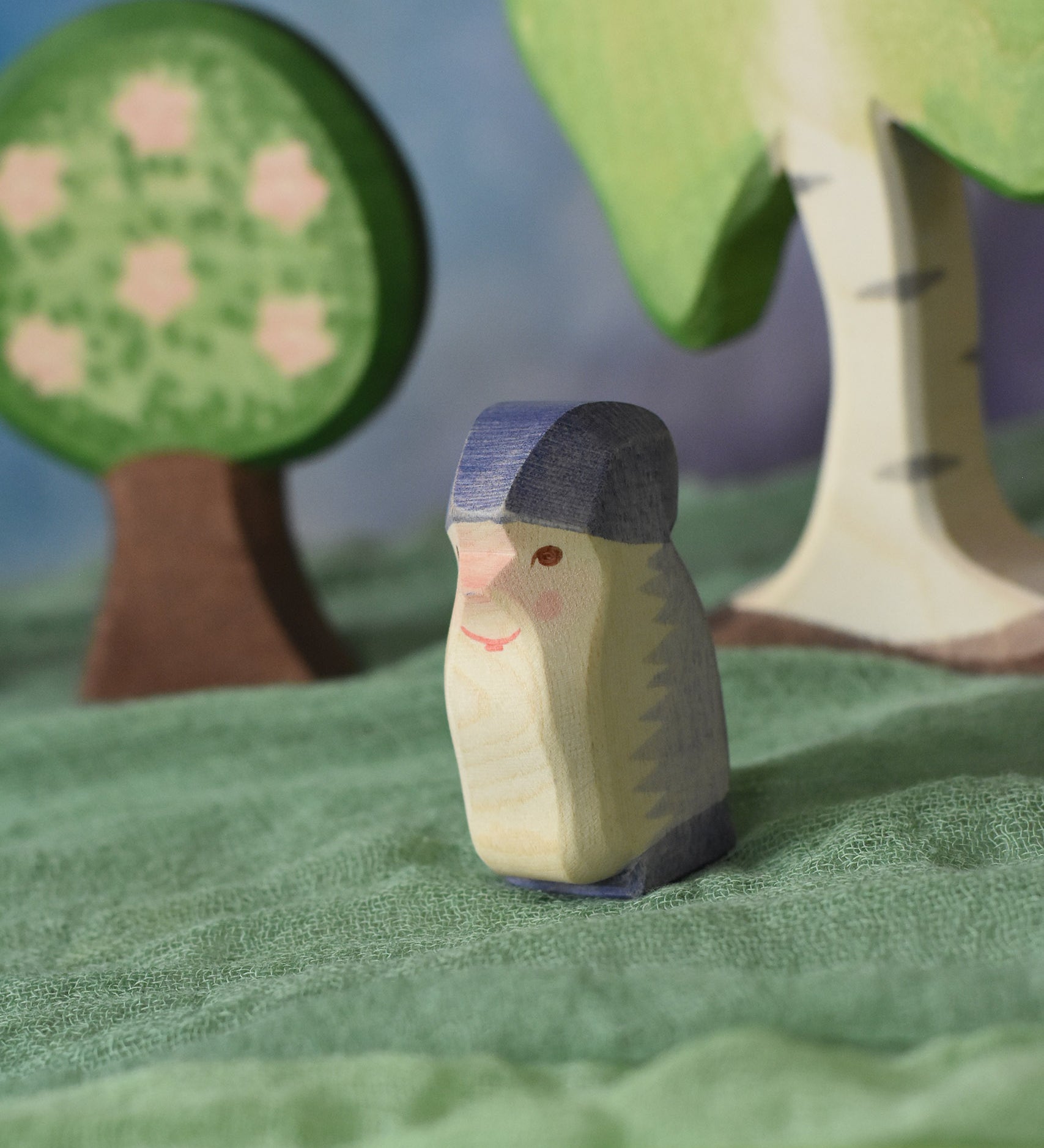 An Ostheimer purple dwarf wooden toy figure placed in a small world play scene. The dwarf figure has a purple coloured outfit with matching hat and a long white beard. The figure has been placed on a green coloured Ostheimer play scarf. These wooden figures are part of a large range of expertly hand crafted, Waldorf inspired, wooden toys here at Babipur.