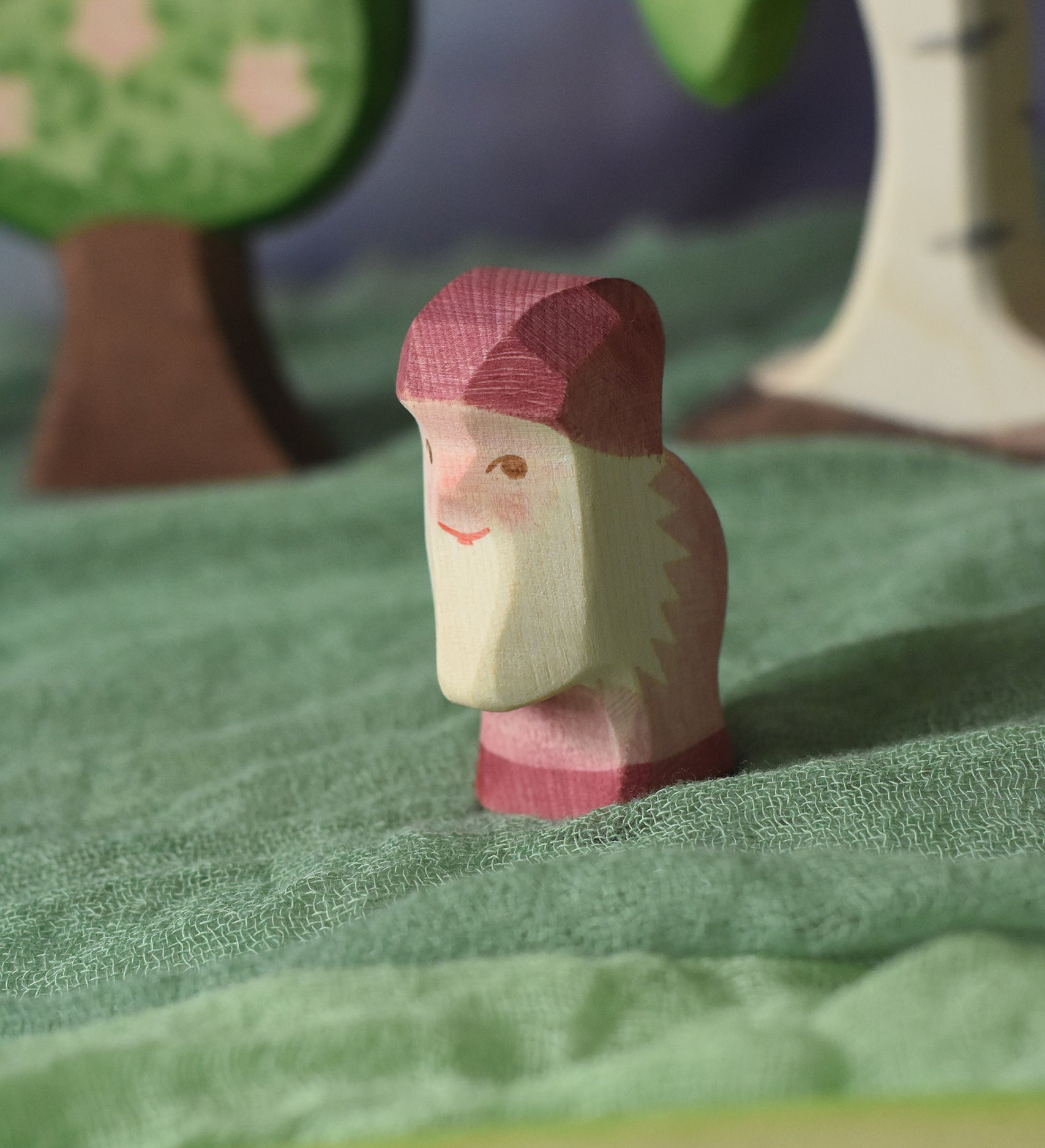 An Ostheimer violet dwarf wooden toy figure placed in a small world play scene. The dwarf figure has a violet coloured outfit with matching hat and a white beard. The figure has been placed on a green coloured Ostheimer play scarf. These wooden figures are part of a large range of expertly hand crafted, Waldorf inspired, wooden toys here at Babipur.