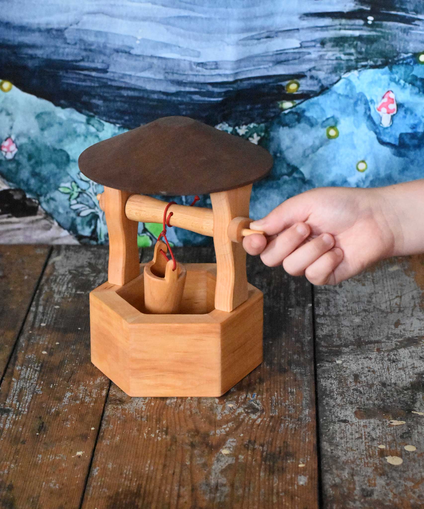 A child's hand winding up the bucket on the Ostheimer wooden wishing well toy. These wooden figures are part of a wide range of expertly hand crafted wooden toys here at Babipur.