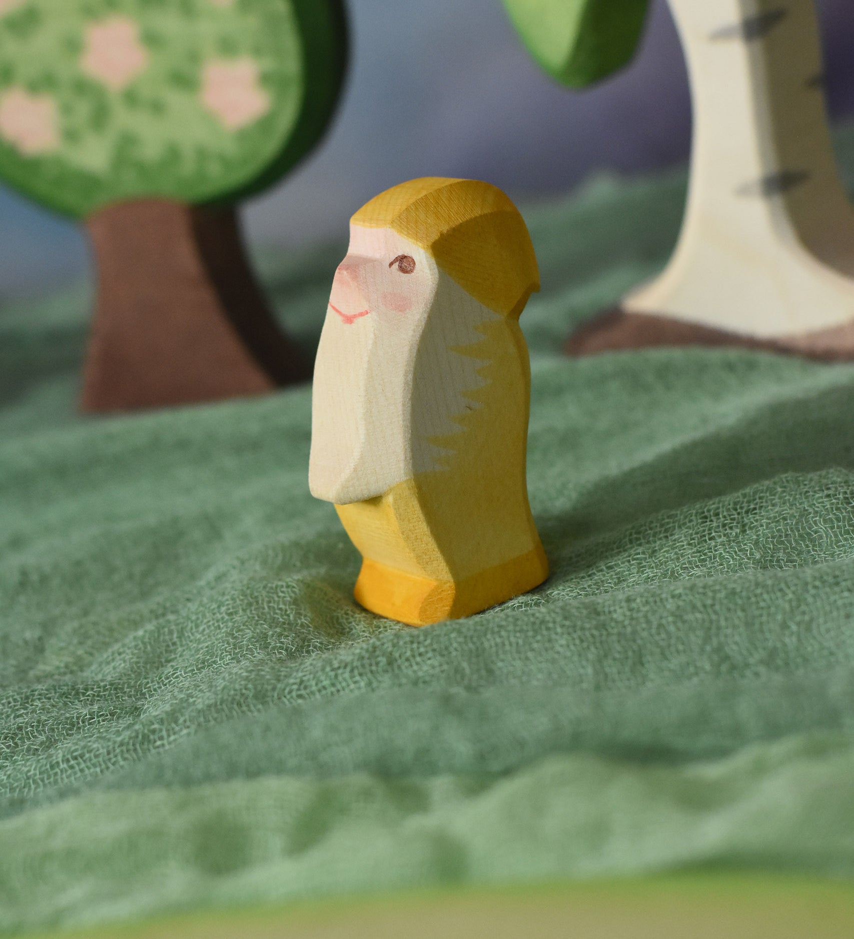 An Ostheimer yellow dwarf wooden toy figure placed in a small world play scene. The dwarf figure has a yellow coloured outfit with matching hat and a long white beard. The figure has been placed on a green coloured Ostheimer play scarf. This wooden figure is part of a large range of expertly hand crafted, Waldorf inspired, wooden toys here at Babipur.
