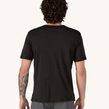 A man wearing the Patagonia Men's Capilene Cool Merino Graphic Shirt with a Heritage Header design in Black. The man is facing away from the camera. showing the back of the t-shirt.
