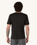 A man wearing the Patagonia Men's Capilene Cool Merino Graphic Shirt with a Heritage Header design in Black. The man is facing away from the camera. showing the back of the t-shirt.