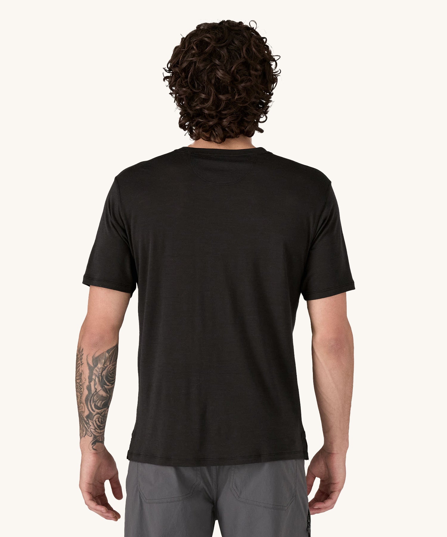 A man wearing the Patagonia Men's Capilene Cool Merino Graphic Shirt with a Heritage Header design in Black. The man is facing away from the camera. showing the back of the t-shirt.