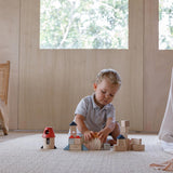 A child playing with the PlanToys Creative Blocks in the Orchard colour way. The child is sitting on a rug.