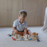 A child playing with the PlanToys Creative Blocks in the Orchard colour way. The child is sitting on a rug.