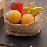 Plan Toys Fruit Produce Set - wooden toy Apples, Oranges & Bananas shown in a jute sack in a play kitchen.