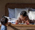 Two children playing with the PlanToys Mini Cars Set. One child is laying on a bed the other is standing up at the end of the bed.