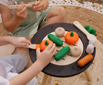A close up of children playing with the Plan Toys Vegetable Produce Set containing wooden Cucumbers, Onions & Pumpkin play food on a wooden toy grill.