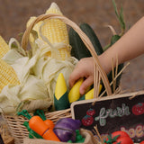 Child's hand reaching for corn on the cob paly food from the Plan Toys Wooden Vegetable Produce Set.