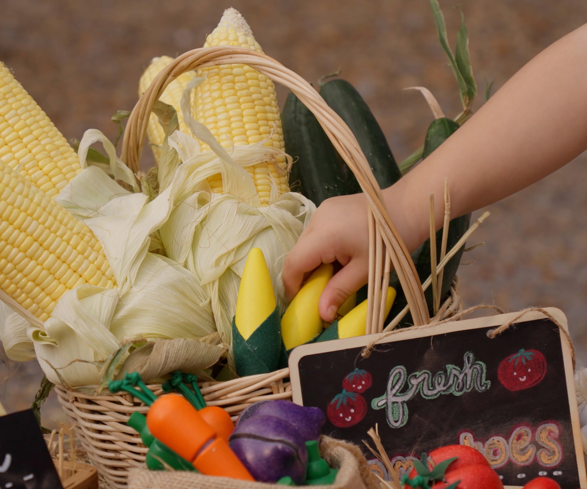Child's hand reaching for corn on the cob paly food from the Plan Toys Wooden Vegetable Produce Set.