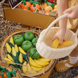 A child placing a wooden toy banana into a basket from the Plan Toys Fruit Produce Set - Apples, Oranges & Bananas.