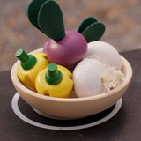 Bowl in a play kitchen filled with vegetable play food from the PlanToys wooden produce set - yellow peppers, radish and garlic.