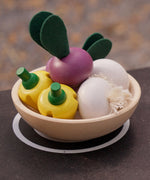 Bowl in a play kitchen filled with vegetable play food from the PlanToys wooden produce set - yellow peppers, radish and garlic.